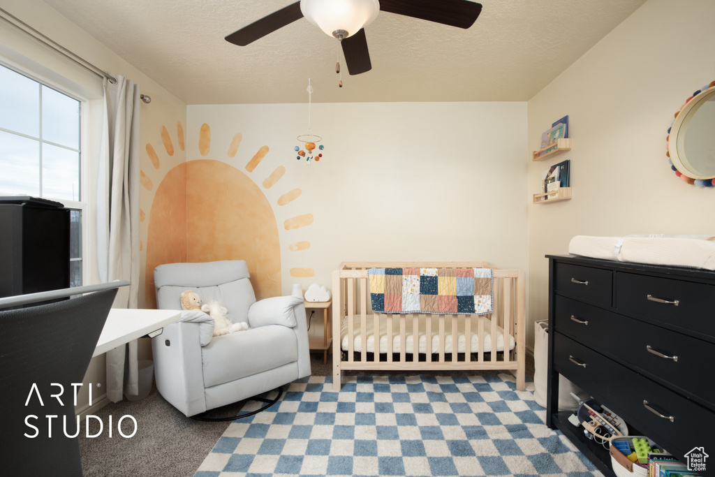Carpeted bedroom featuring a textured ceiling, ceiling fan, and a crib
