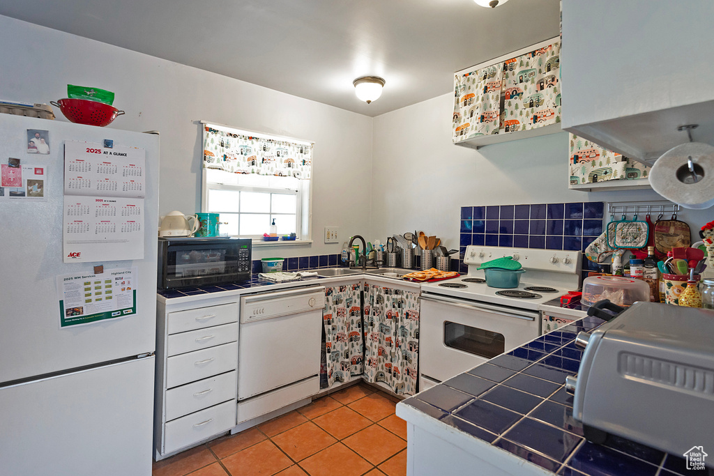 Kitchen featuring white appliances, tile counters, white cabinetry, a sink, and light tile patterned flooring