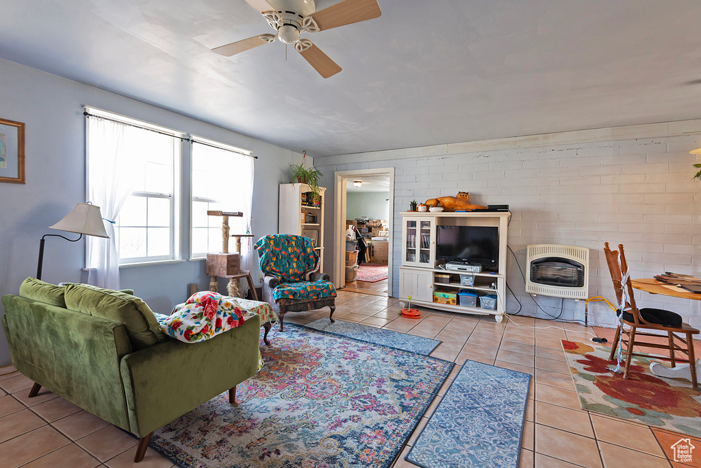 Tiled living area featuring brick wall, a fireplace, a ceiling fan, and heating unit