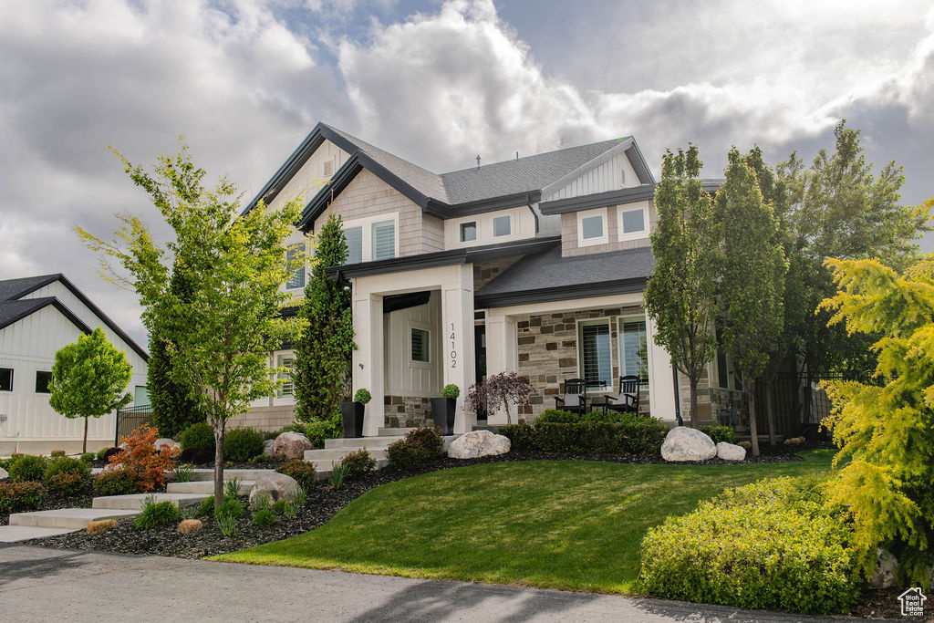 Craftsman-style house with stone siding, a front yard, board and batten siding, and covered porch