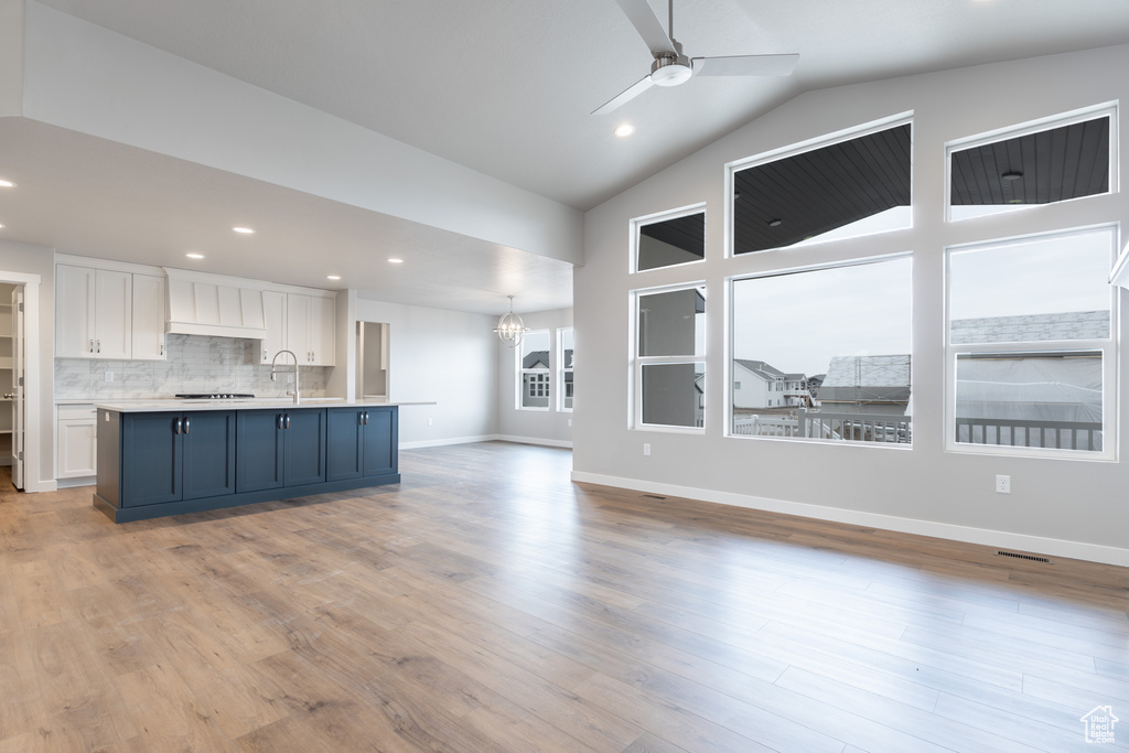 Unfurnished living room with light wood-style flooring, recessed lighting, ceiling fan with notable chandelier, a sink, and baseboards