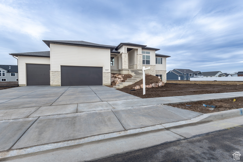 Prairie-style home featuring an attached garage, stone siding, driveway, and a residential view