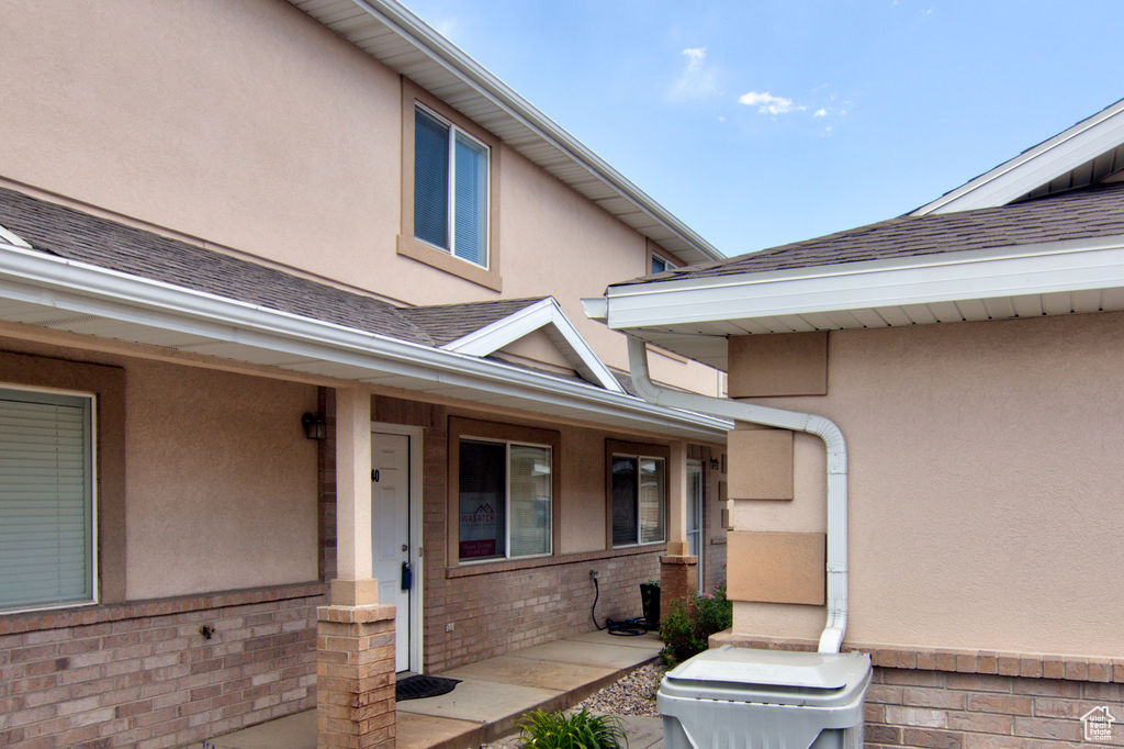 Doorway to property with stucco siding, covered porch, roof with shingles, and brick siding
