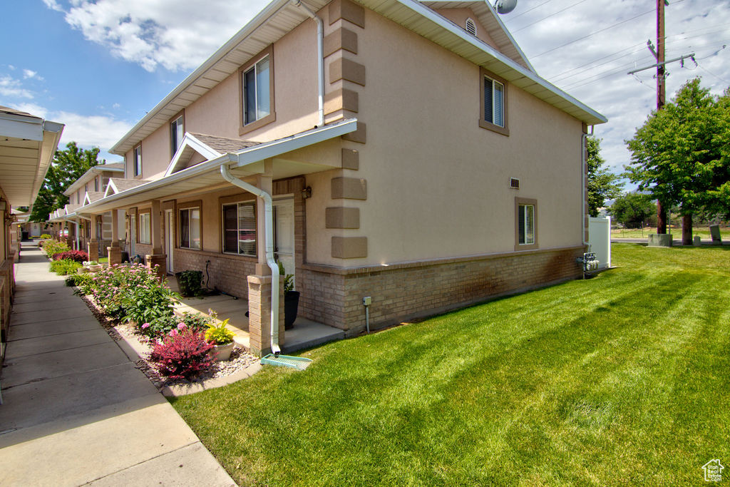 View of side of property featuring stucco siding, brick siding, a lawn, and a porch