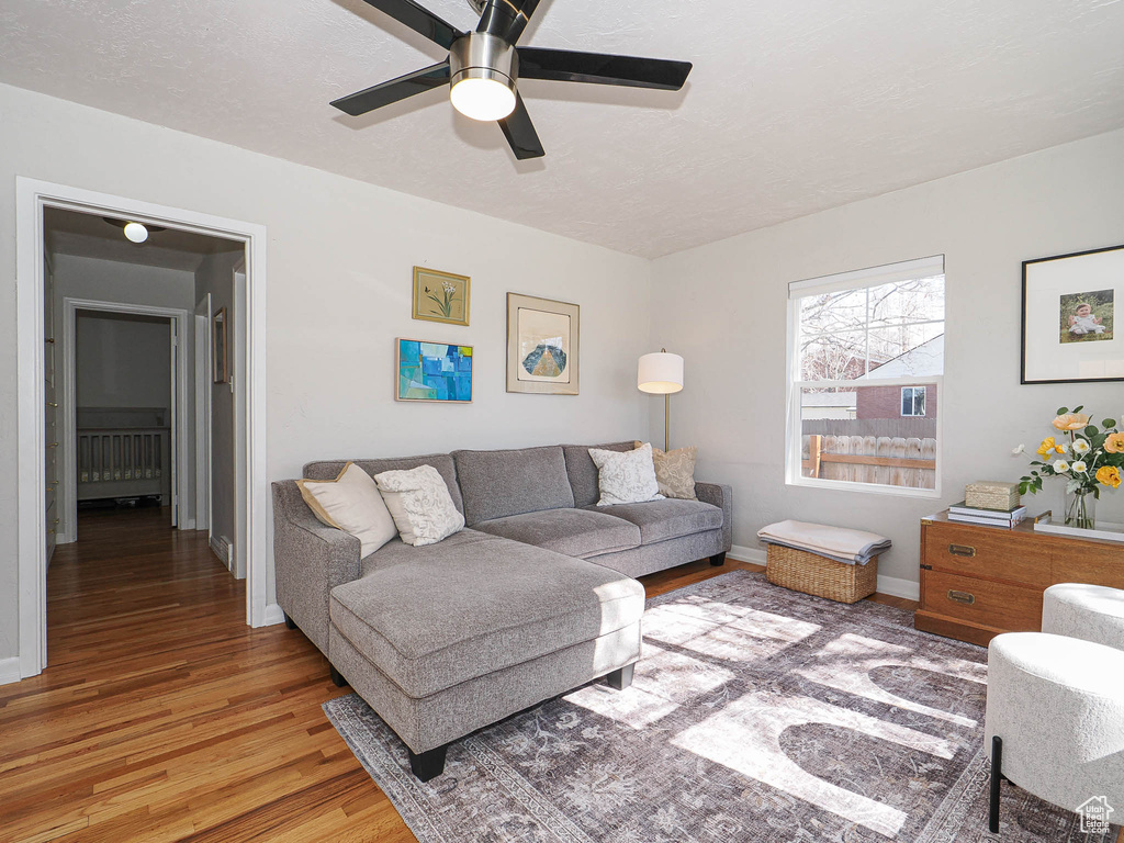 Living room featuring ceiling fan, a textured ceiling, baseboards, and wood finished floors