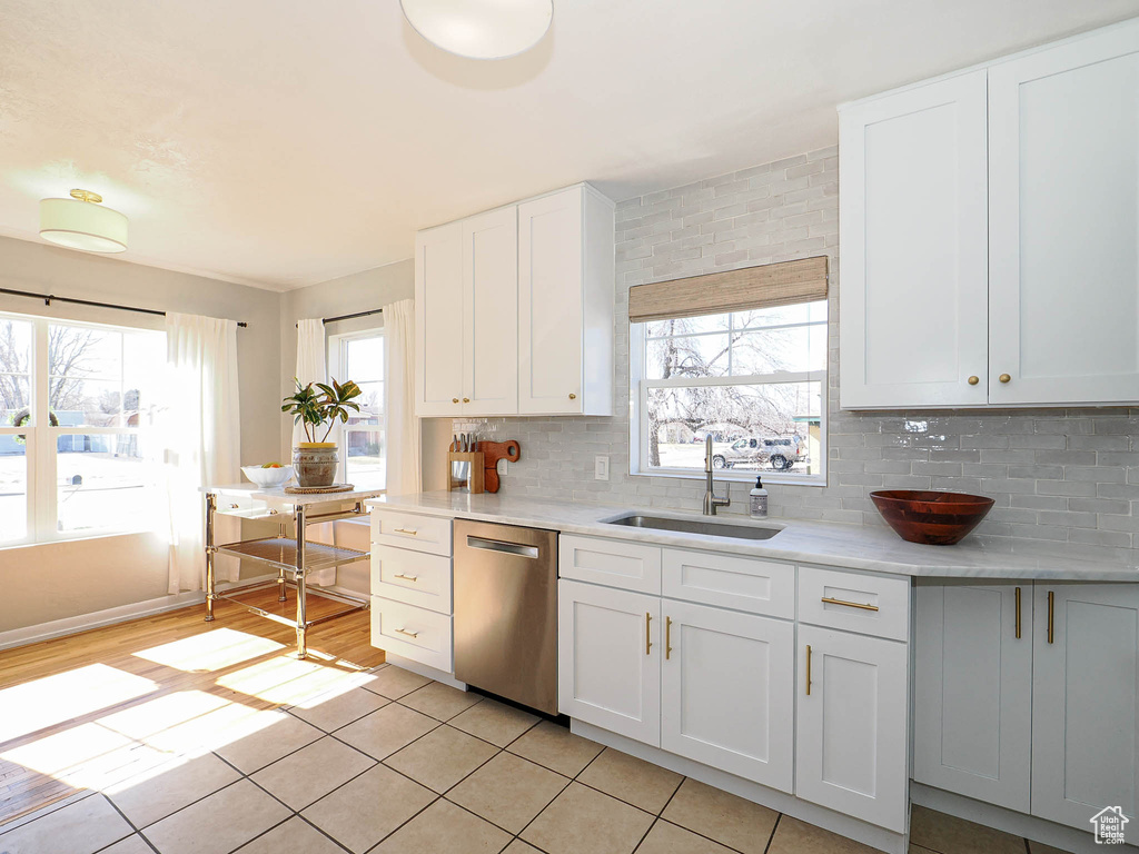 Kitchen featuring dishwasher, backsplash, light countertops, white cabinetry, and a sink