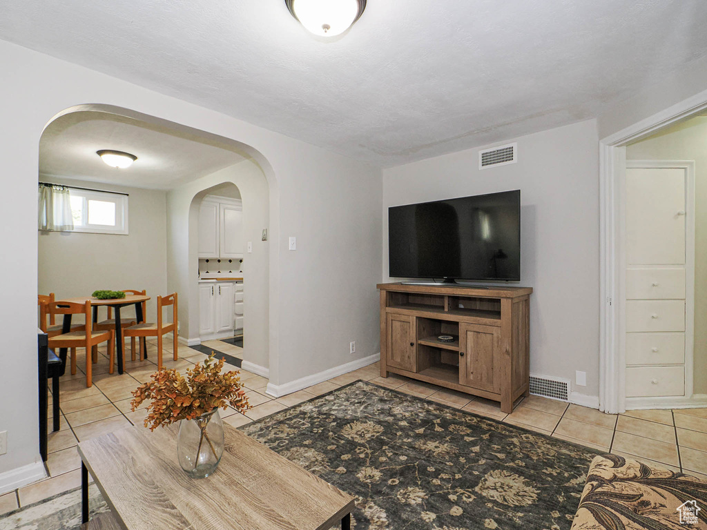 Living room featuring arched walkways, light tile patterned floors, visible vents, and baseboards