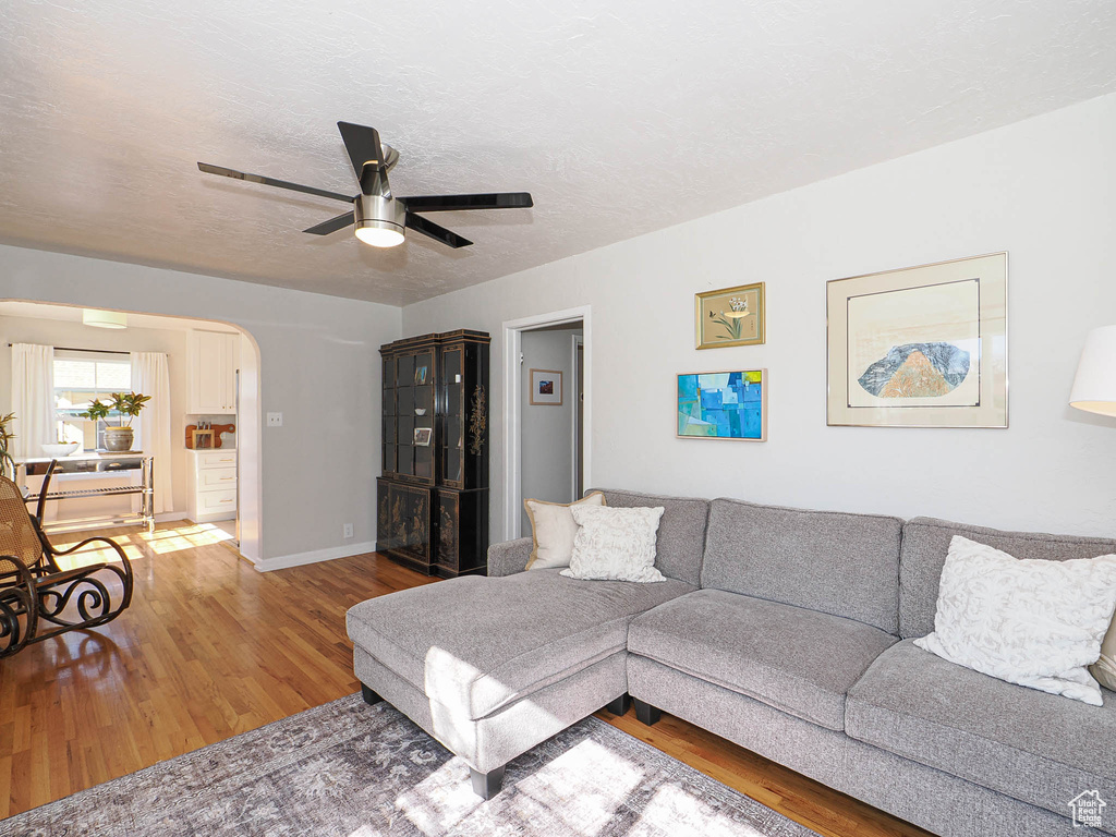 Living room with arched walkways, a textured ceiling, wood finished floors, a ceiling fan, and baseboards