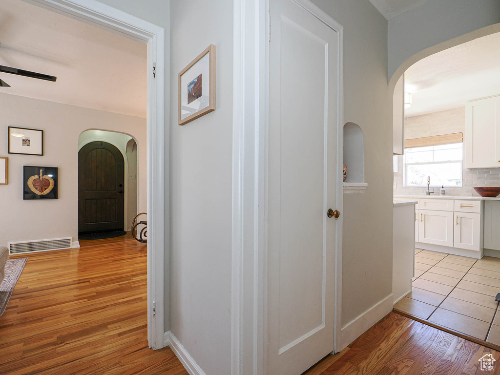 Hallway featuring arched walkways, light wood-style flooring, a sink, visible vents, and baseboards