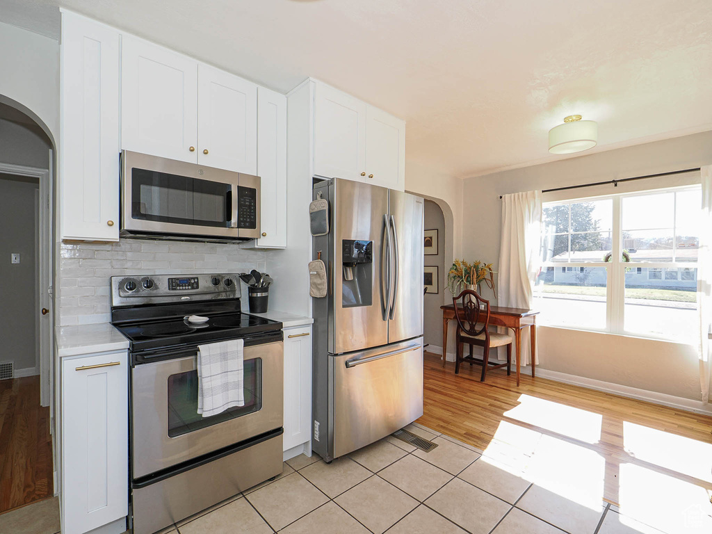 Kitchen with arched walkways, light countertops, decorative backsplash, appliances with stainless steel finishes, and white cabinetry