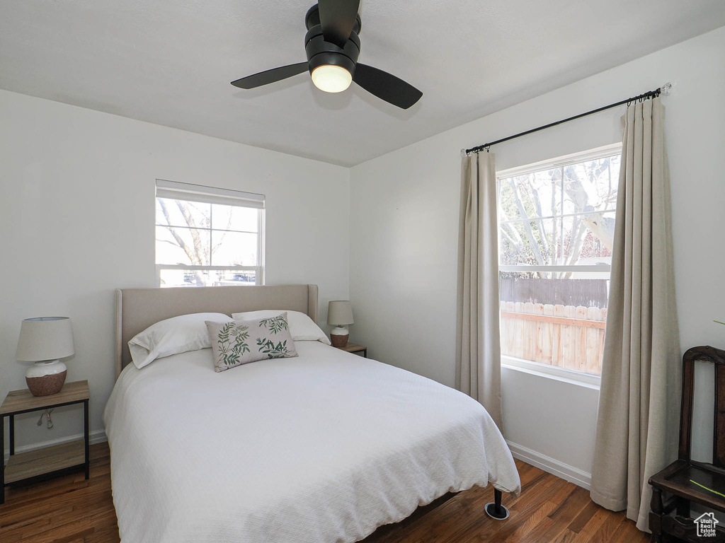 Bedroom with ceiling fan, multiple windows, baseboards, and dark wood-type flooring