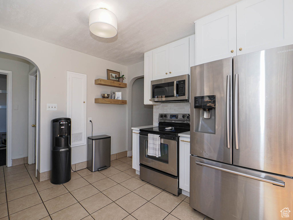 Kitchen featuring arched walkways, open shelves, appliances with stainless steel finishes, and white cabinetry
