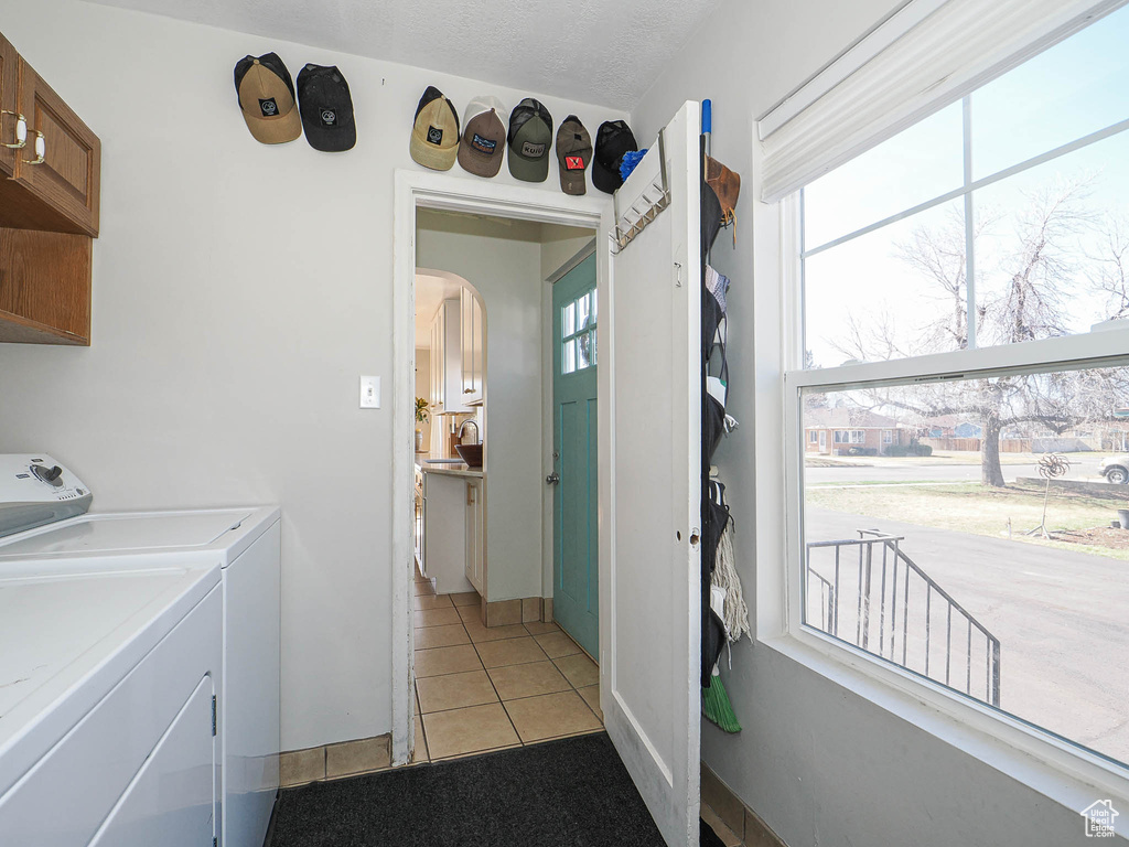 Laundry room featuring arched walkways, light tile patterned floors, a textured ceiling, cabinet space, and washing machine and clothes dryer