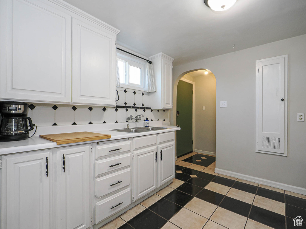Kitchen featuring arched walkways, light countertops, decorative backsplash, white cabinets, and a sink