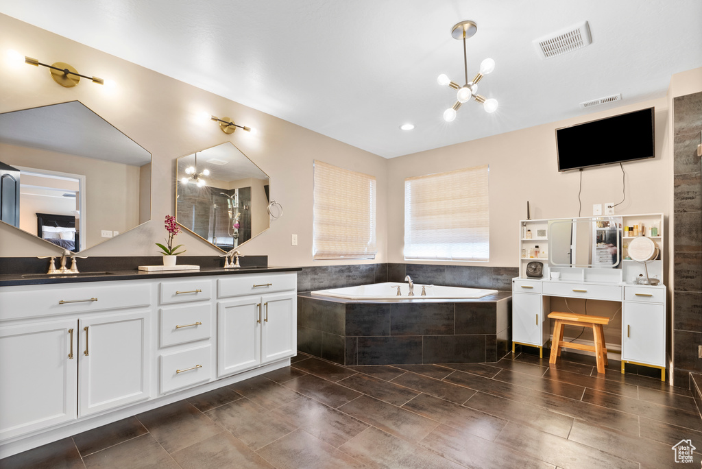 Full bathroom featuring a garden tub, a sink, visible vents, double vanity, and an inviting chandelier