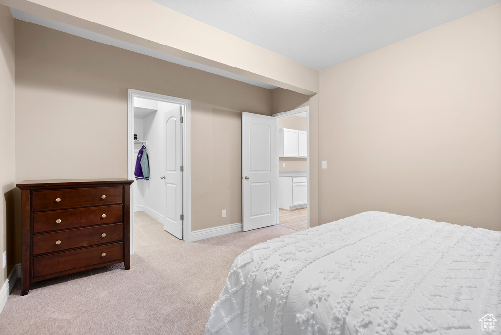 Bedroom featuring light carpet, a walk in closet, and baseboards