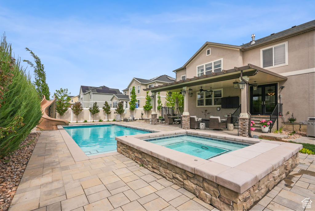 View of pool with a water slide, an in-ground hot tub, a patio, a ceiling fan, and a fenced backyard