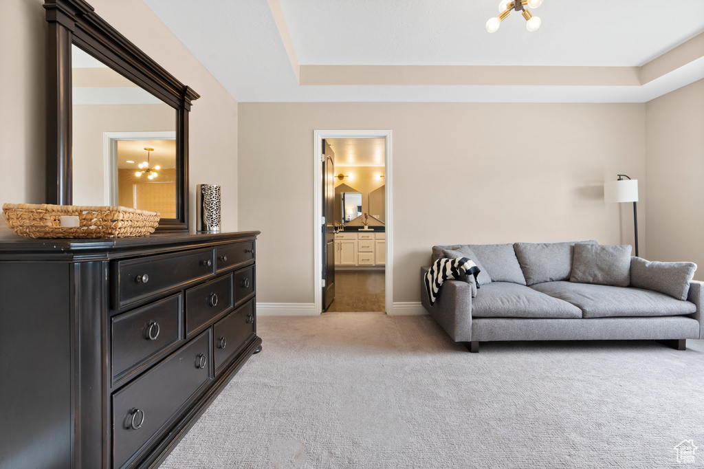 Living room with a tray ceiling, light colored carpet, baseboards, and an inviting chandelier