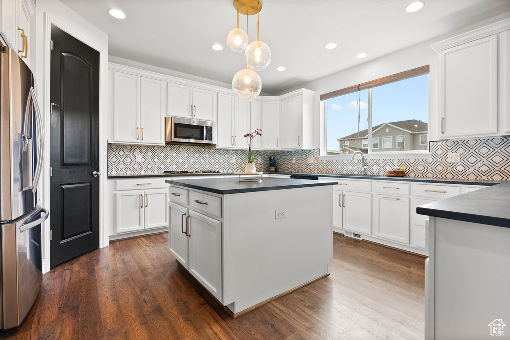 Kitchen with stainless steel appliances, white cabinets, dark wood-style floors, dark countertops, and decorative light fixtures