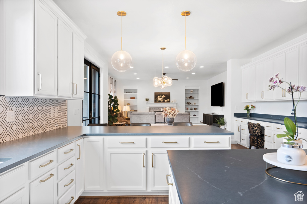 Kitchen featuring tasteful backsplash, white cabinets, dark countertops, open floor plan, and hanging light fixtures