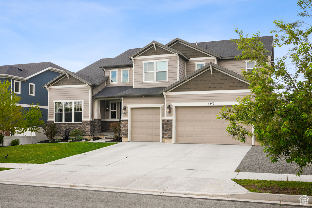 Craftsman house with concrete driveway, stone siding, a front yard, and an attached garage
