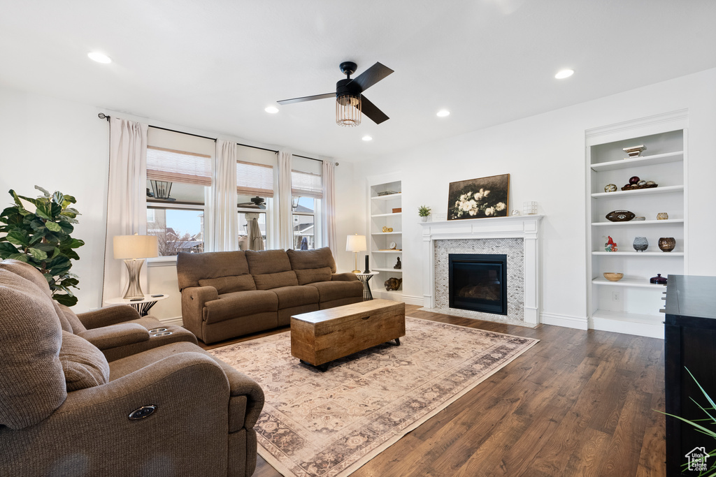 Living room with a fireplace with flush hearth, ceiling fan, dark wood-type flooring, built in shelves, and recessed lighting