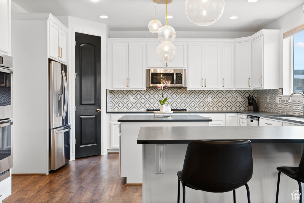 Kitchen featuring hanging light fixtures, appliances with stainless steel finishes, dark countertops, and white cabinets