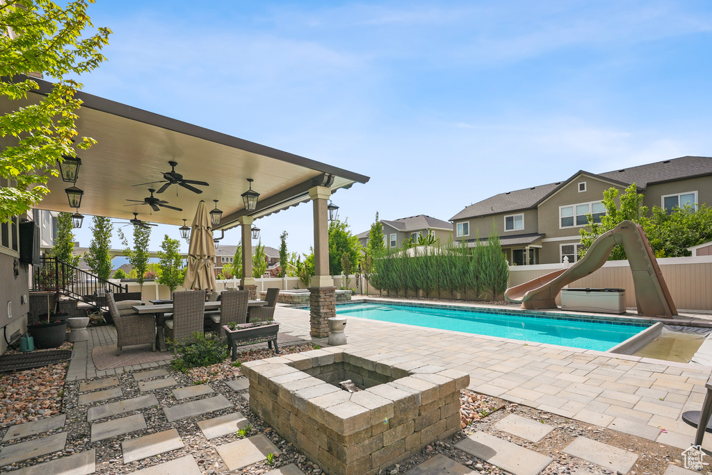 View of pool featuring a water slide, a fire pit, a patio area, a ceiling fan, and a residential view