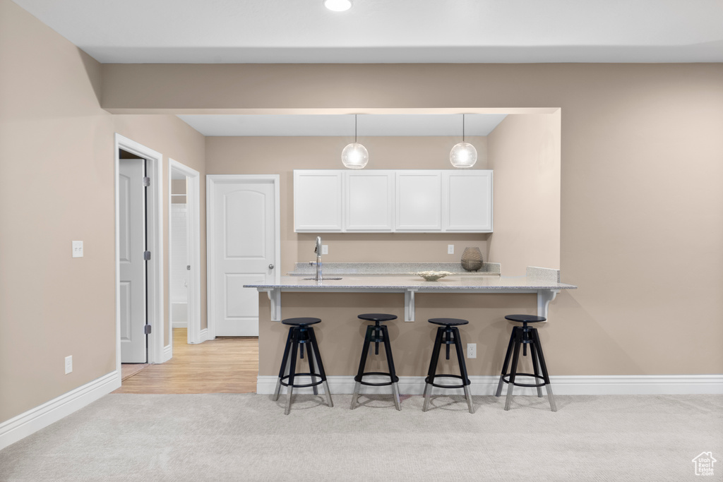 Kitchen with white cabinets, a sink, light carpet, a kitchen breakfast bar, and baseboards