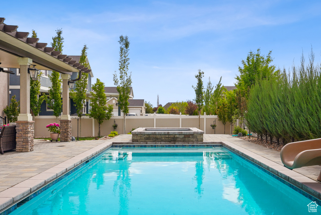 View of pool featuring a water slide, a fenced backyard, a patio area, and an in-ground hot tub