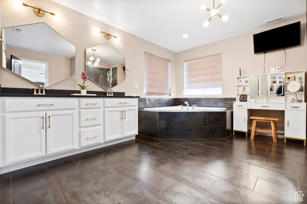 Full bathroom featuring double vanity, visible vents, a garden tub, a notable chandelier, and a sink