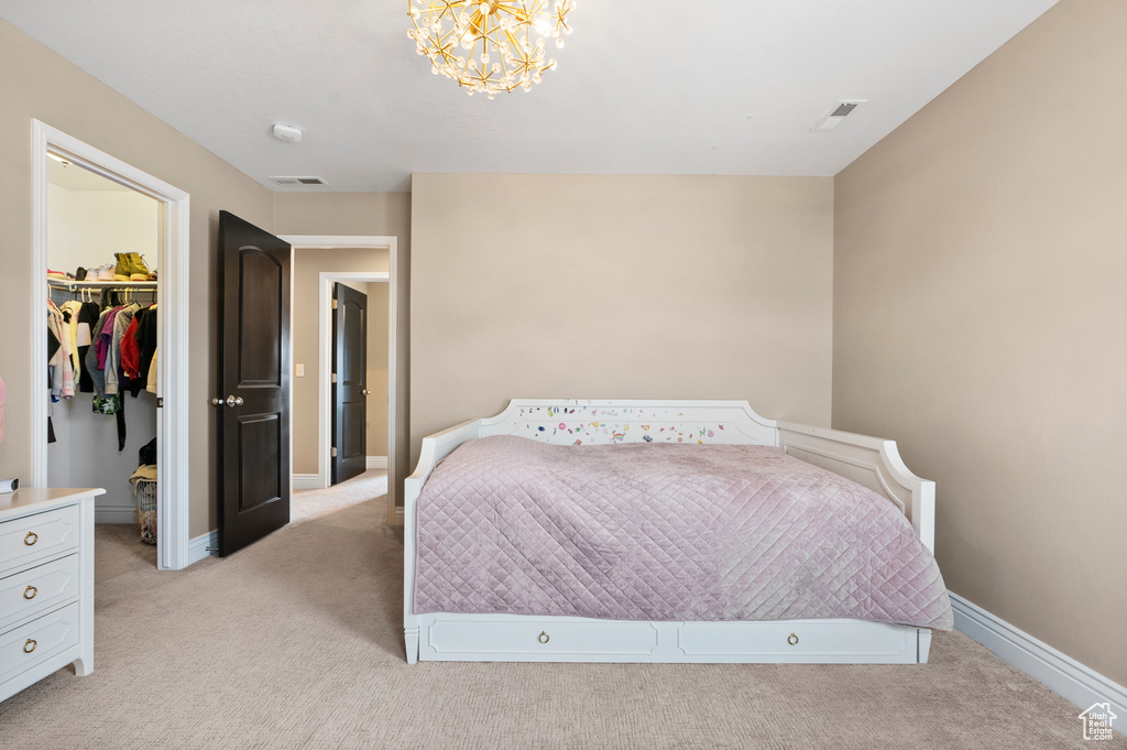 Bedroom featuring a walk in closet, a notable chandelier, light colored carpet, visible vents, and baseboards