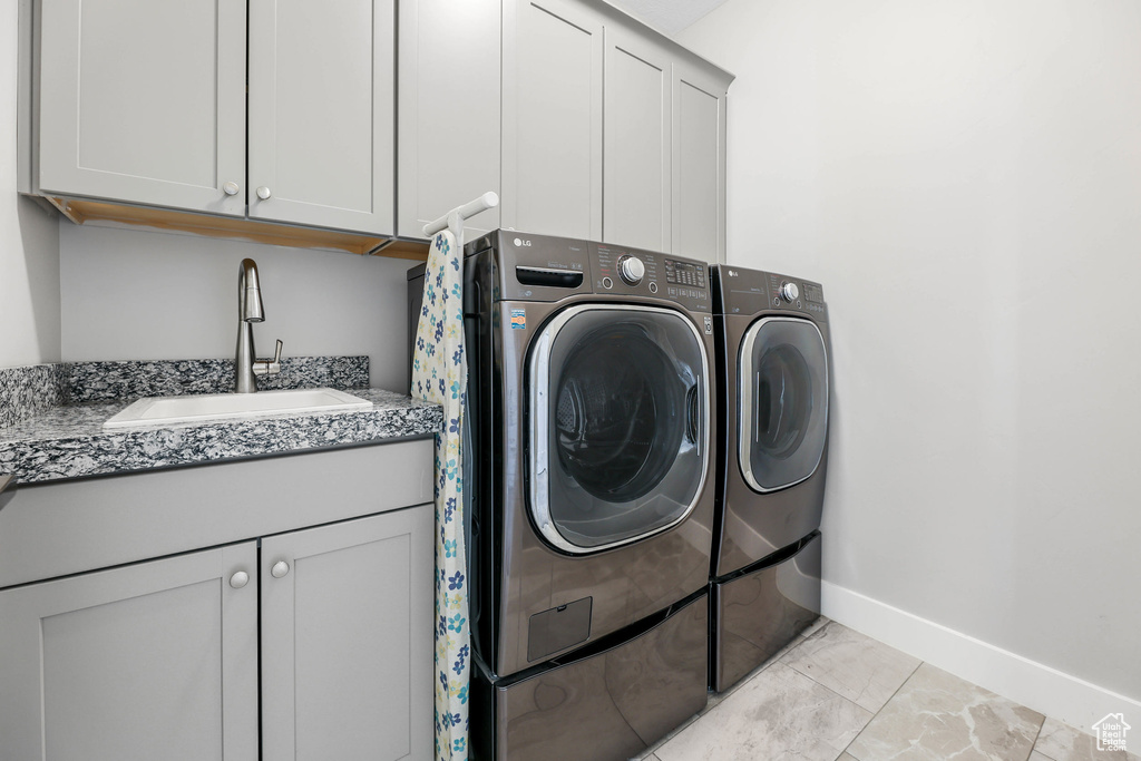 Clothes washing area featuring washing machine and clothes dryer, a sink, cabinet space, and baseboards