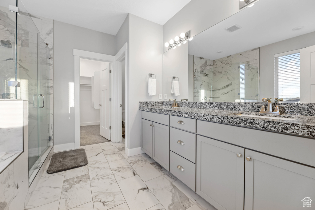 Bathroom featuring baseboards, marble finish floor, a spacious closet, a marble finish shower, and double vanity