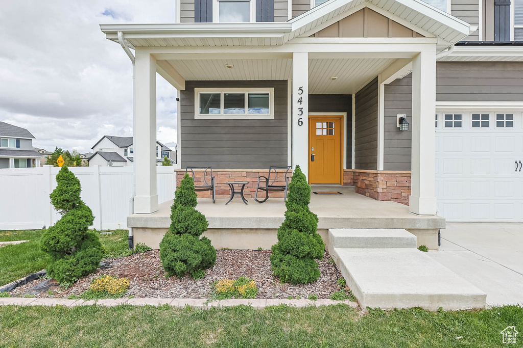 Entrance to property featuring covered porch, fence, board and batten siding, and stone siding