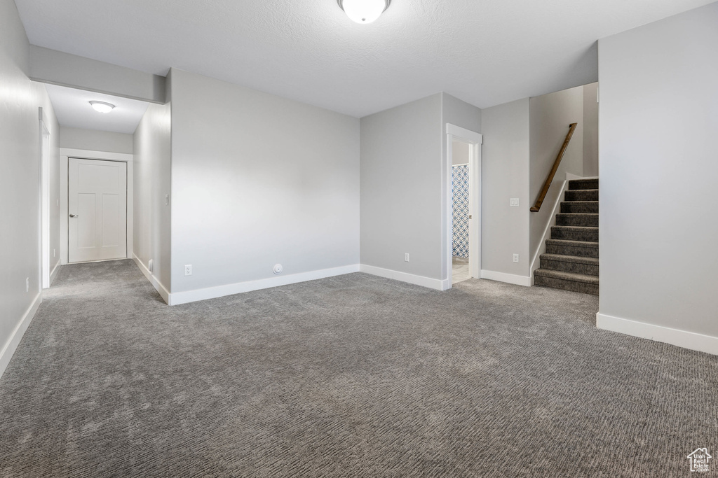 Carpeted spare room featuring stairway and baseboards
