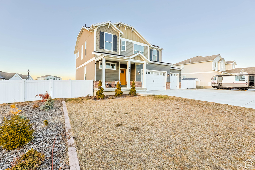 Craftsman-style home with driveway, an attached garage, covered porch, fence, and board and batten siding