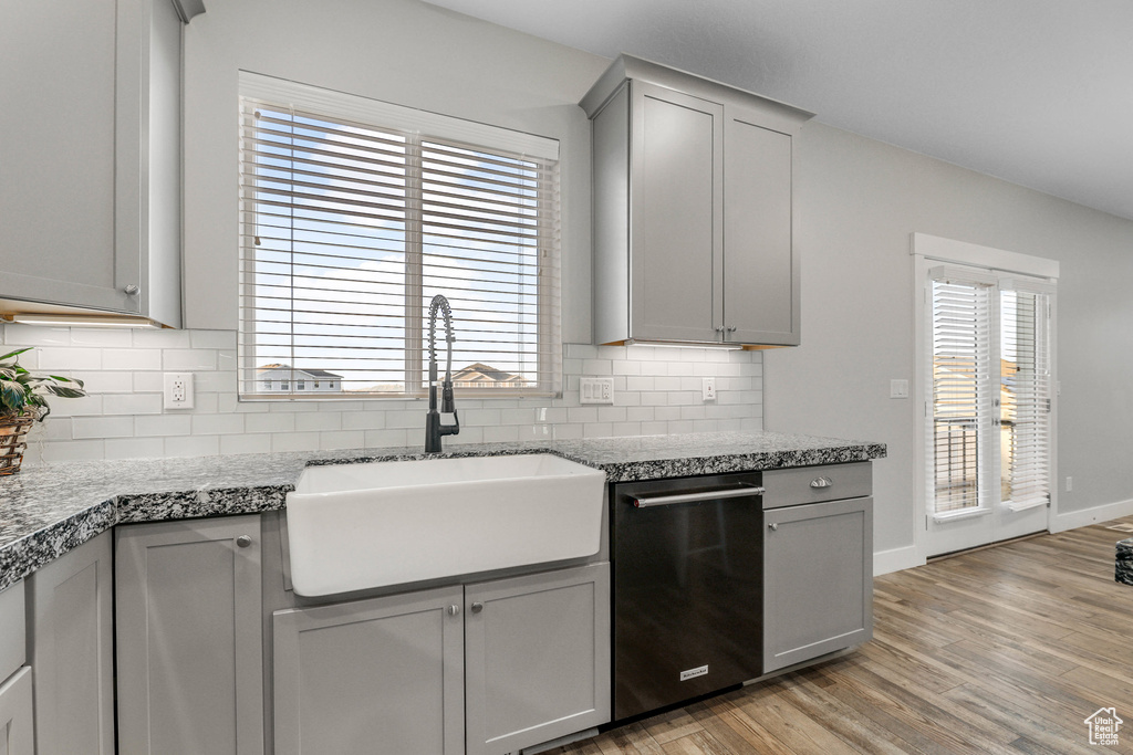 Kitchen with black dishwasher, a healthy amount of sunlight, gray cabinetry, light wood-type flooring, and a sink