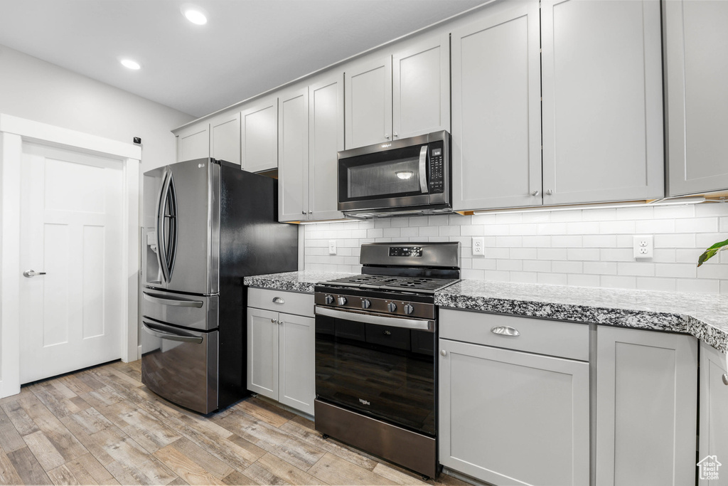 Kitchen with light stone counters, recessed lighting, appliances with stainless steel finishes, light wood finished floors, and tasteful backsplash