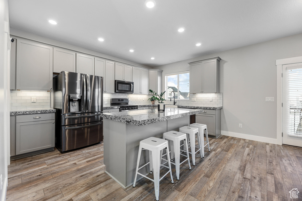 Kitchen featuring gray cabinetry, appliances with stainless steel finishes, a kitchen bar, and a center island