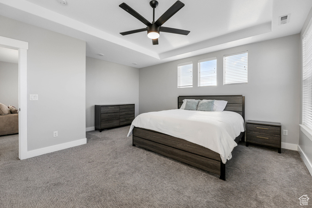 Bedroom featuring light carpet, baseboards, visible vents, a ceiling fan, and a tray ceiling
