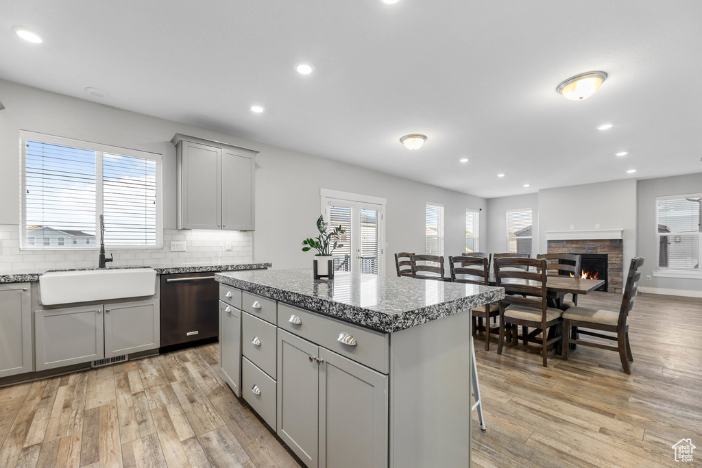 Kitchen with dishwasher, light stone counters, a center island, gray cabinets, and a sink