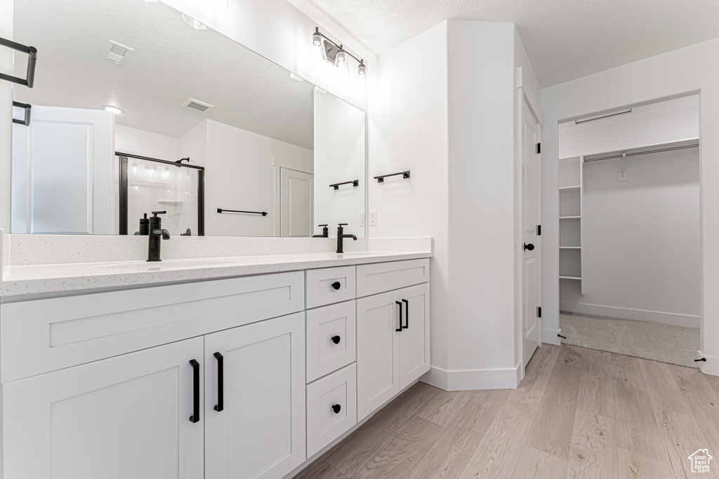 Bathroom featuring a stall shower, double vanity, wood finished floors, a spacious closet, and baseboards