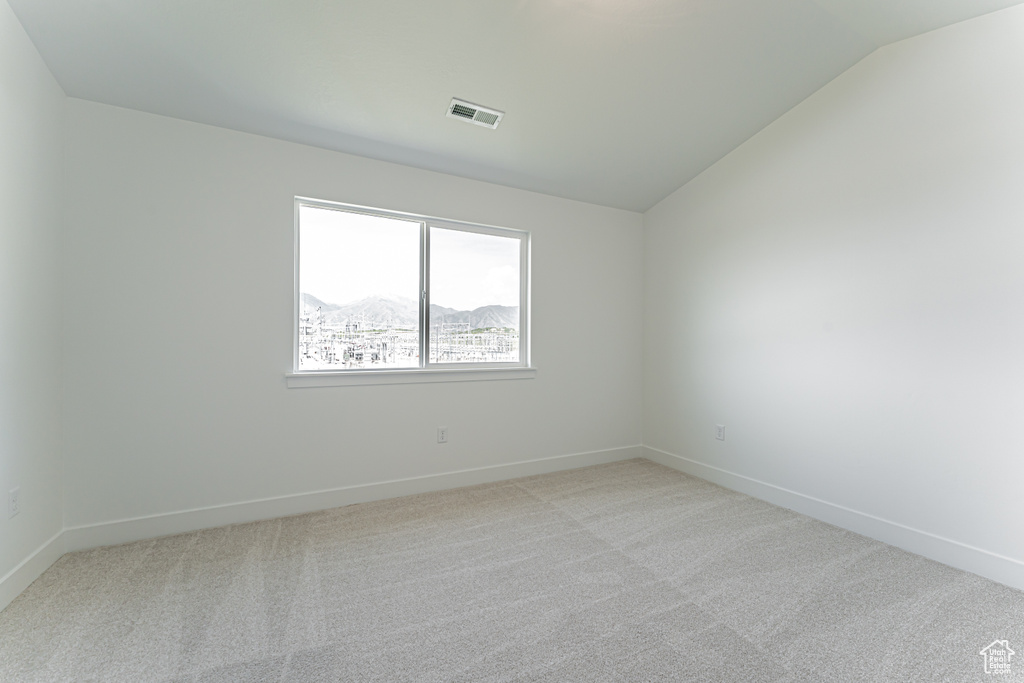 Carpeted empty room featuring lofted ceiling and baseboards