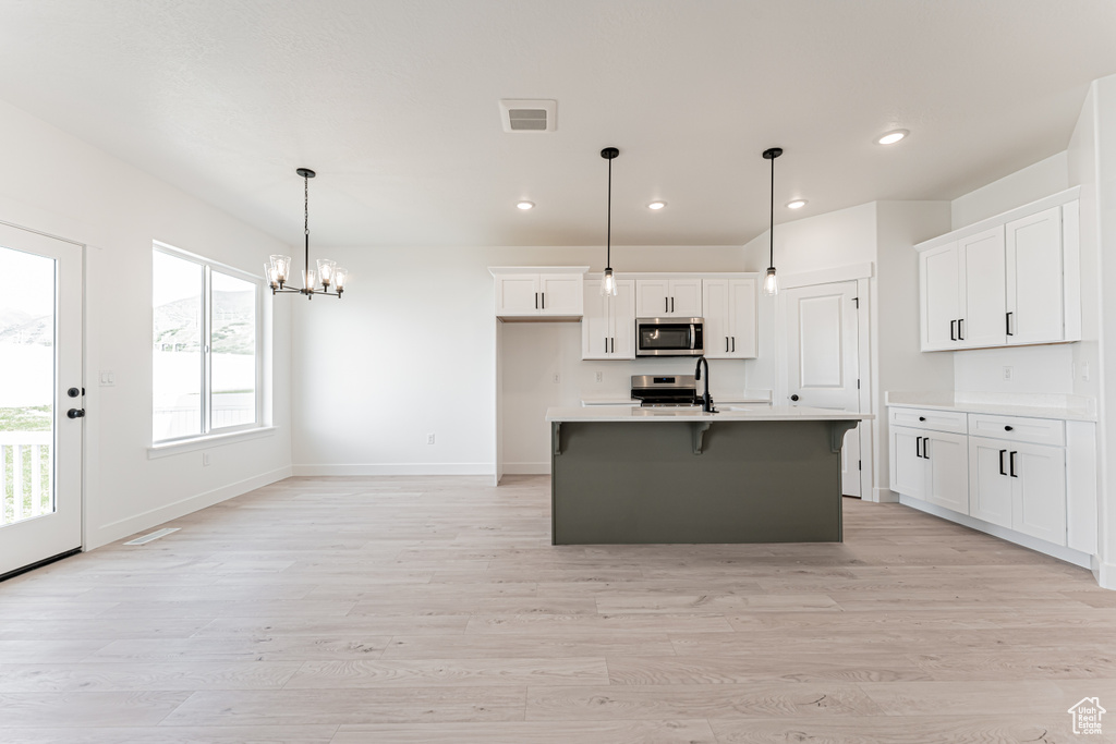 Kitchen with appliances with stainless steel finishes, recessed lighting, light wood-style flooring, white cabinets, and a chandelier
