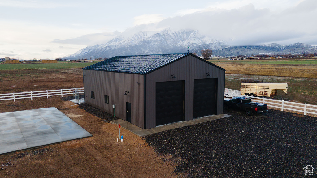 View of outbuilding with a rural view, fence, a mountain view, and an outdoor structure