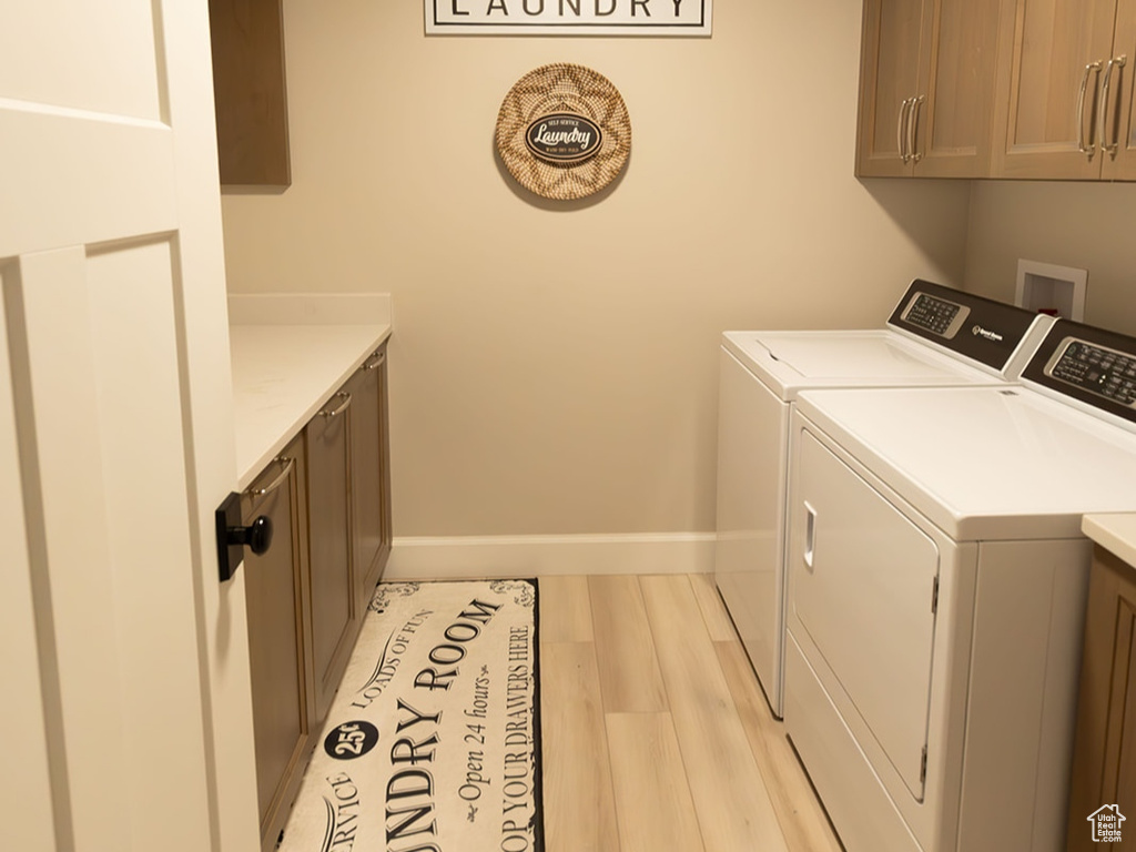 Laundry room with light wood finished floors, washing machine and dryer, cabinet space, and baseboards
