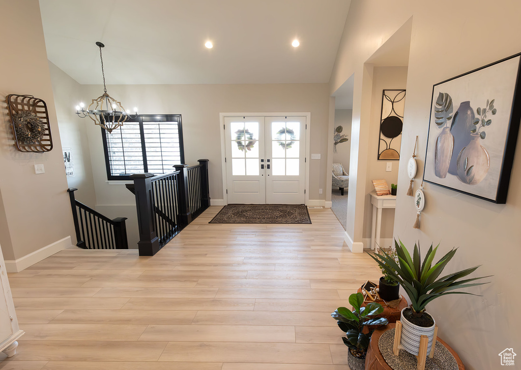 Foyer featuring lofted ceiling, a chandelier, light wood-style flooring, baseboards, and french doors