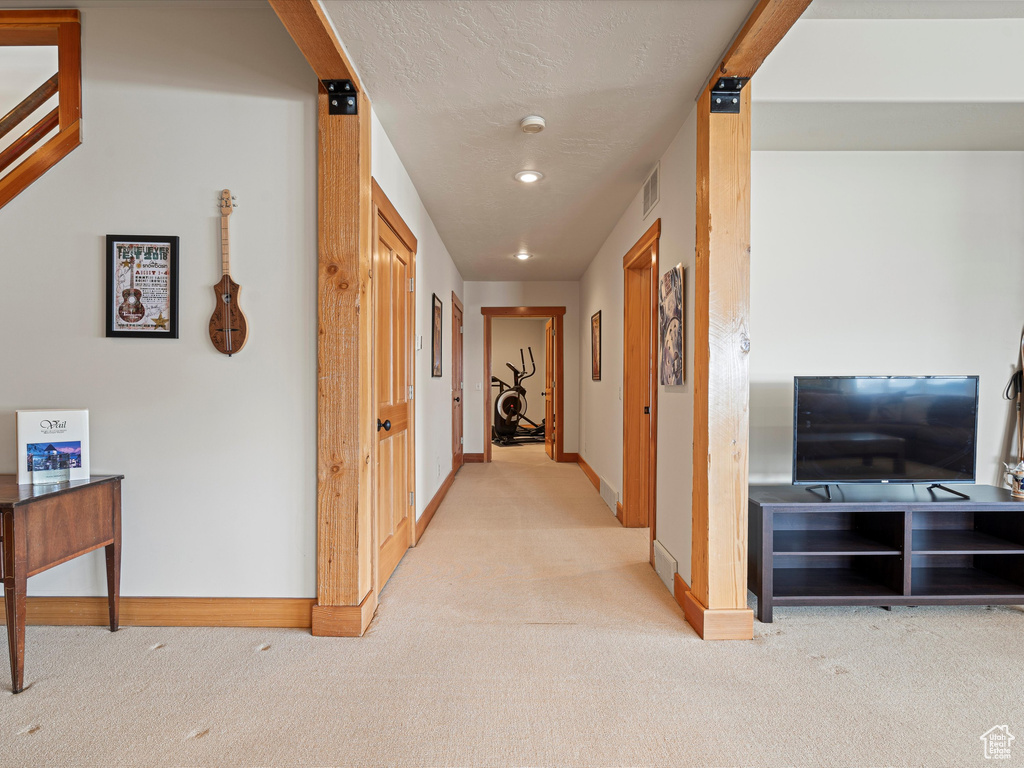 Corridor featuring light carpet, baseboards, visible vents, and a textured ceiling