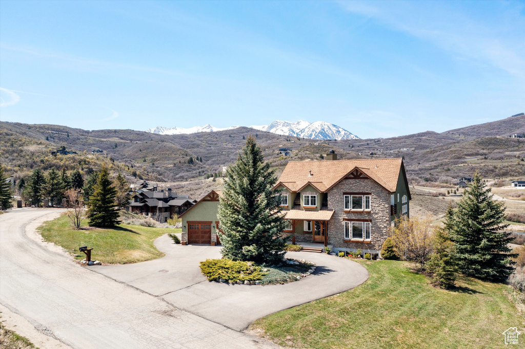 View of front facade with a front yard, a mountain view, driveway, stone siding, and a chimney